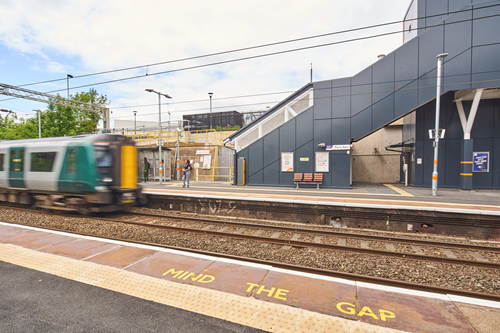 A photo taken from one of the platforms of Perry Barr railway station looking across to the other platform, where there is a passenger stood waiting for a train